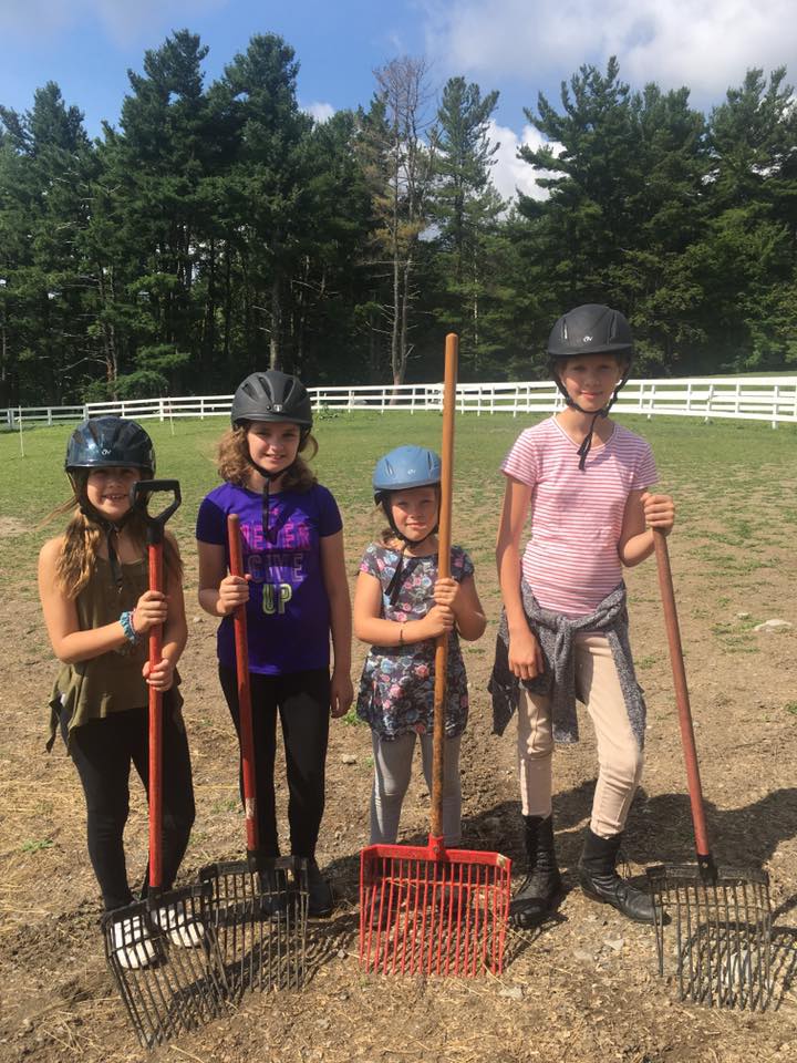 Four young girls wearing helmets in a field with pitchforks participate in High & Mighty's barn program in Ghent, NY